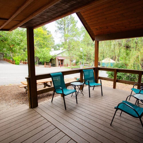 A wooden porch with four blue patio chairs overlooks a quiet street and trees in a residential neighborhood.