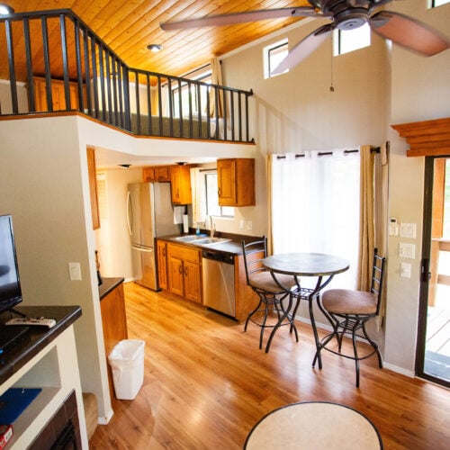 Interior shot of a loft cabin with kitchen, dining area, and stairs.